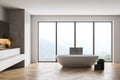 Light wooden bathroom with white bathtub and towels near window on parquet floor