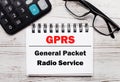 On a light wooden table calculator, glasses and a blank notepad with the text GPRS General Packet Radio Service . Business concept