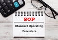 On a light wooden table calculator, glasses and a blank notepad with the text SOP Standard Operating Procedure. Business concept