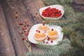 A light wooden table top with a plate of freshly baked muffins decorated with red berries sprinkled with white powder and a plate