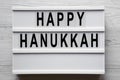 Lightbox with `Happy Hanukkah` word over white wooden surface, overhead view. From above, flat-lay