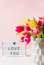 Lightbox with love you message and blurred fresh spring yellow and pink tulips bouquet in vase on white wooden table Royalty Free Stock Photo