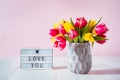 Lightbox with love you message and fresh spring yellow and pink tulips bouquet in a vase on white wooden table with pink Royalty Free Stock Photo