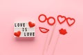 Lightbox with slogan LOVE HAS NO GENDER, red paper props glasses and lips on pastel pink background