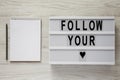 Lightbox with text `Follow you heart`, blank notepad over white wooden surface. Valentine Day 14 February