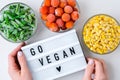 Lightbox with text GO VEGAN Three Bowls of frozen vegetables food of yellow corn, green beans, red tomatoes. Colors of traffic