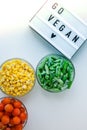 Lightbox with text GO VEGAN Three Bowls of frozen vegetables food of yellow corn, green beans, red tomatoes. Colors of traffic