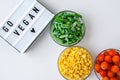 Lightbox with text GO VEGAN Three Bowls of frozen vegetables food of yellow corn, green beans, red tomatoes. Colors of