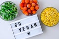 Lightbox with text GO VEGAN Three Bowls of frozen vegetables food of yellow corn, green beans, red tomatoes. Colors of