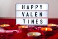 Lightbox with text HAPPY VALENTINES and Burning red candles on confetti sequinned background with feathers. Saint Valentines Day Royalty Free Stock Photo