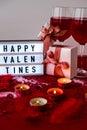 Lightbox with text HAPPY VALENTINES two glasses of red wine and gift boxes Burning red candles on confetti sequinned background Royalty Free Stock Photo