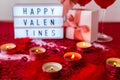 Lightbox with text HAPPY VALENTINES two glasses of red wine and gift boxes Burning red candles on confetti sequinned background