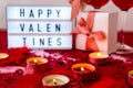 Lightbox with text HAPPY VALENTINES two glasses of red wine and gift boxes Burning red candles on confetti sequinned background Royalty Free Stock Photo