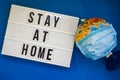 Lightbox with text STAY AT HOME World globe with medical face mask on blue background