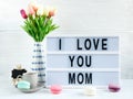 Lightbox with title Ilove you mom and tender tulips, macaroons on white wooden background. Mothers day decoration concept.