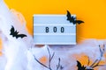 Lightbox with word BOO and halloween party decorations. Bats on dry tree branch with spider net for Halloween on orange