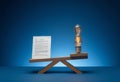 A lightbulb and a document positioned on opposite ends of a wooden balance scale, set against a blue gradient background. Royalty Free Stock Photo