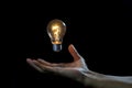Lightbulb on hand black background, magic idea energy concept