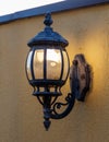 A lighted lamp post with a yellow wall behind it Royalty Free Stock Photo
