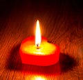 Lighted red candle in the form of a heart on a wooden table_ Royalty Free Stock Photo