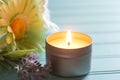 Lighted and Scented votive Candle in a tin holder with flowers on the side, all on teal boards table background with window light Royalty Free Stock Photo