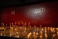 Lighted thin church wax candles standing on a candle table against a red wall