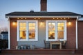 lighted windows of saltbox house at dusk, brick visible