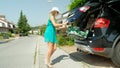 Lighthearted girl`s heavy luggage falls out of big black car when she wants to close the trunk.