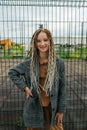 Lighthearted teenage girl with dreads standing in front of a metal fence