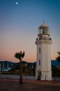 Lighthouse and palm tree on the beach, against the backdrop of mountains. Architectural photography at dusk Royalty Free Stock Photo