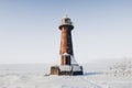 Lighthouse in a calm and desolate winter landscape. A white whitewashed lighthouse over blue sky with clouds