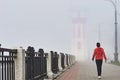 Lighthouse in dense fog. Border between Russia and China. An athletic girl in a red track jacket walks along the embankment