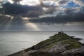 Lighthouse on headland with sun beams over ocean landscape with