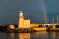 The lighthouse at Howth Harbour in County Dublin bathed in sunlight under a rainbow in front of a stormy sky