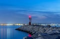 Lighthouse and rocks night seascape. City lights after sunset.