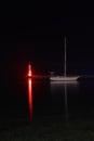 lighthouse and sailboat at dusk. With reflections in the water Royalty Free Stock Photo