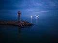 lighthouse on the seashore with red light at night against the background of the lights of the ships