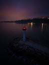 lighthouse on the seashore with red light at night against the background of the lights of the ships