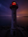 lighthouse on the seashore with red light at night against the background of the lights of the ships