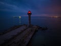 lighthouse on the seashore with red light at night against the background of the lights of the ships