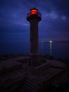 lighthouse on the seashore with red light at night against the background of the lights of the ships