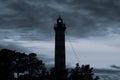 Lighthouse shines in the dark with a dramatic sky. silhouette of glowing beacon in darkness Royalty Free Stock Photo