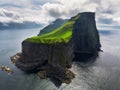 lighthouse sitting on top of a grassy hill close to a rocky black cliff looks over the tranquil sea on cloudy day. Breathtaking