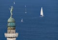 Lighthouse with a statue and a sail boat on the background sea