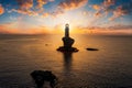 A lighthouse on a steep rock within the calm, mediterranean sea of Greece