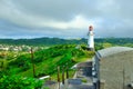 A lighthouse on top of a lush green hill overlooking a town