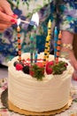 Lighting Birthday Candles on a white cake, decorated with strawberries and berries.