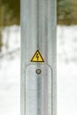 Lighting pole in the city. Electricity service door. Pasted yellow warning sign with lightning. High voltage