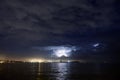 Lightning above the sea or lake at night. Thunderstorm above large industrial city skyline. Royalty Free Stock Photo