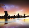 Lightning in cloudy dark sky. Traditional Dutch windmills canal